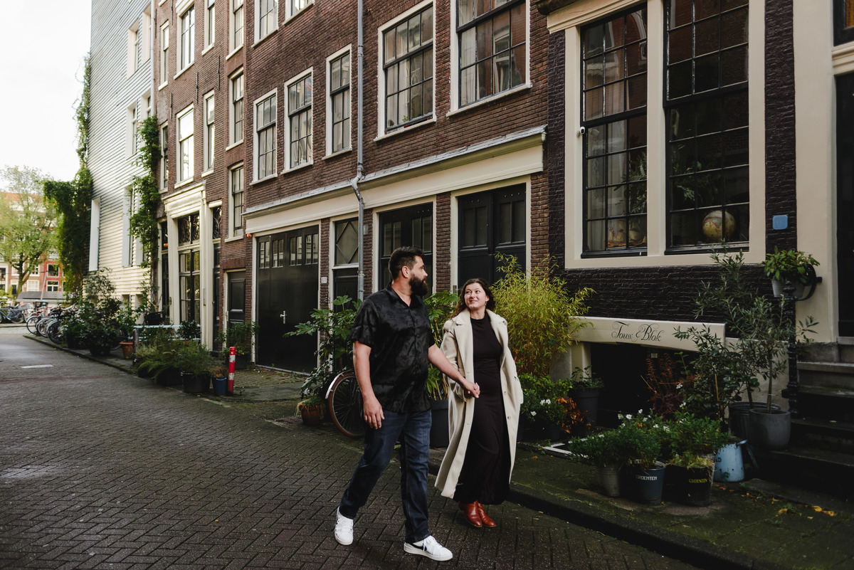 ouple holding hands, strolling through the quiet streets near Oude Waal in Amsterdam, with a historic tower in the background