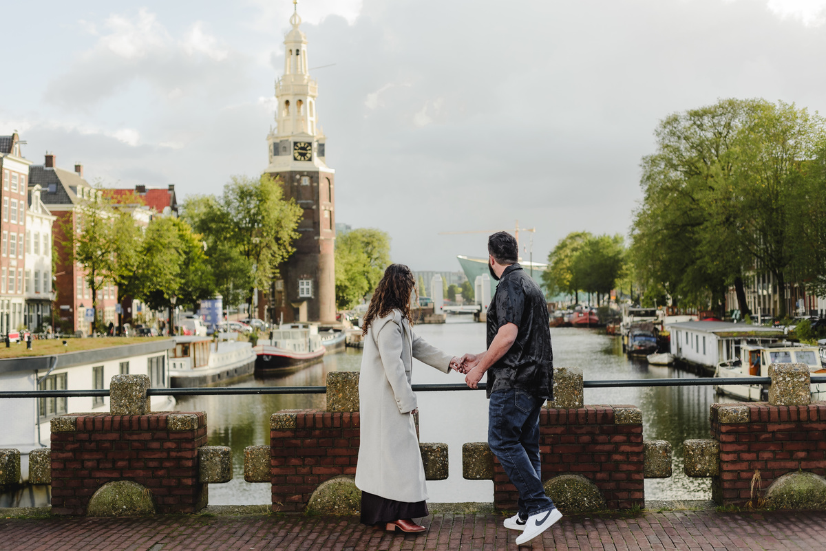 ouple holding hands, strolling through the quiet streets near Oude Waal in Amsterdam, with a historic tower in the background