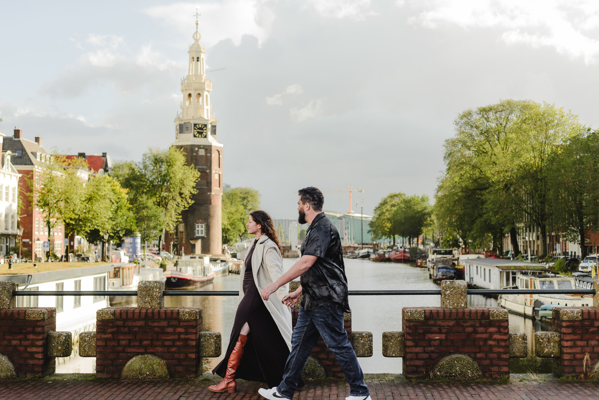 ouple holding hands, strolling through the quiet streets near Oude Waal in Amsterdam, with a historic tower in the background