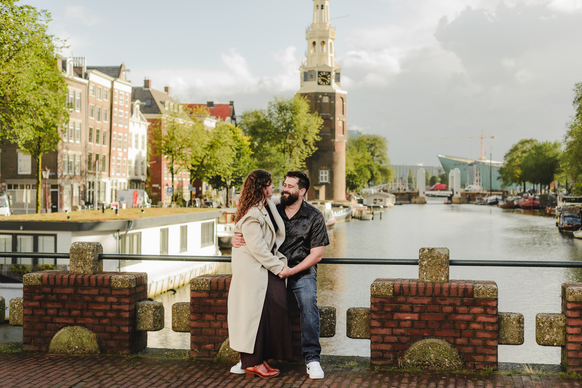 ouple holding hands, strolling through the quiet streets near Oude Waal in Amsterdam, with a historic tower in the background