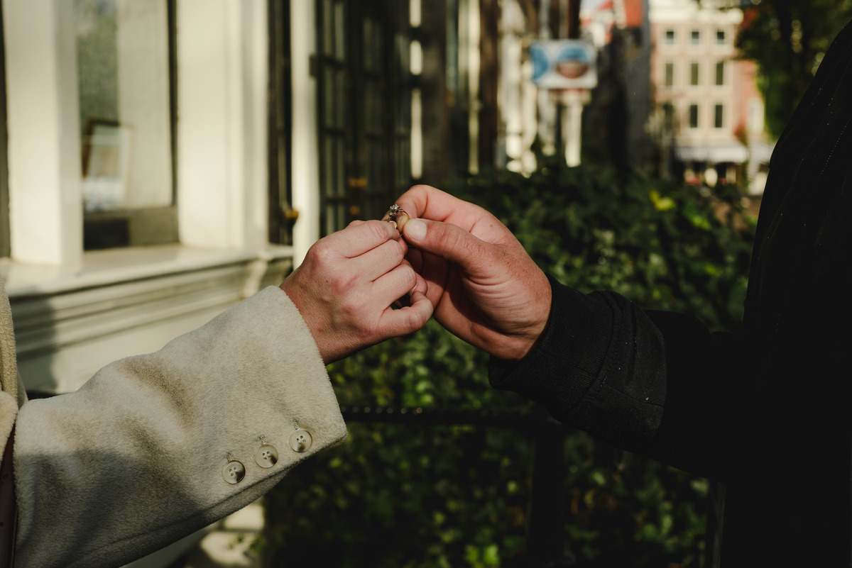 engagement ring held by both hands of the couple with Amsterdam as a background