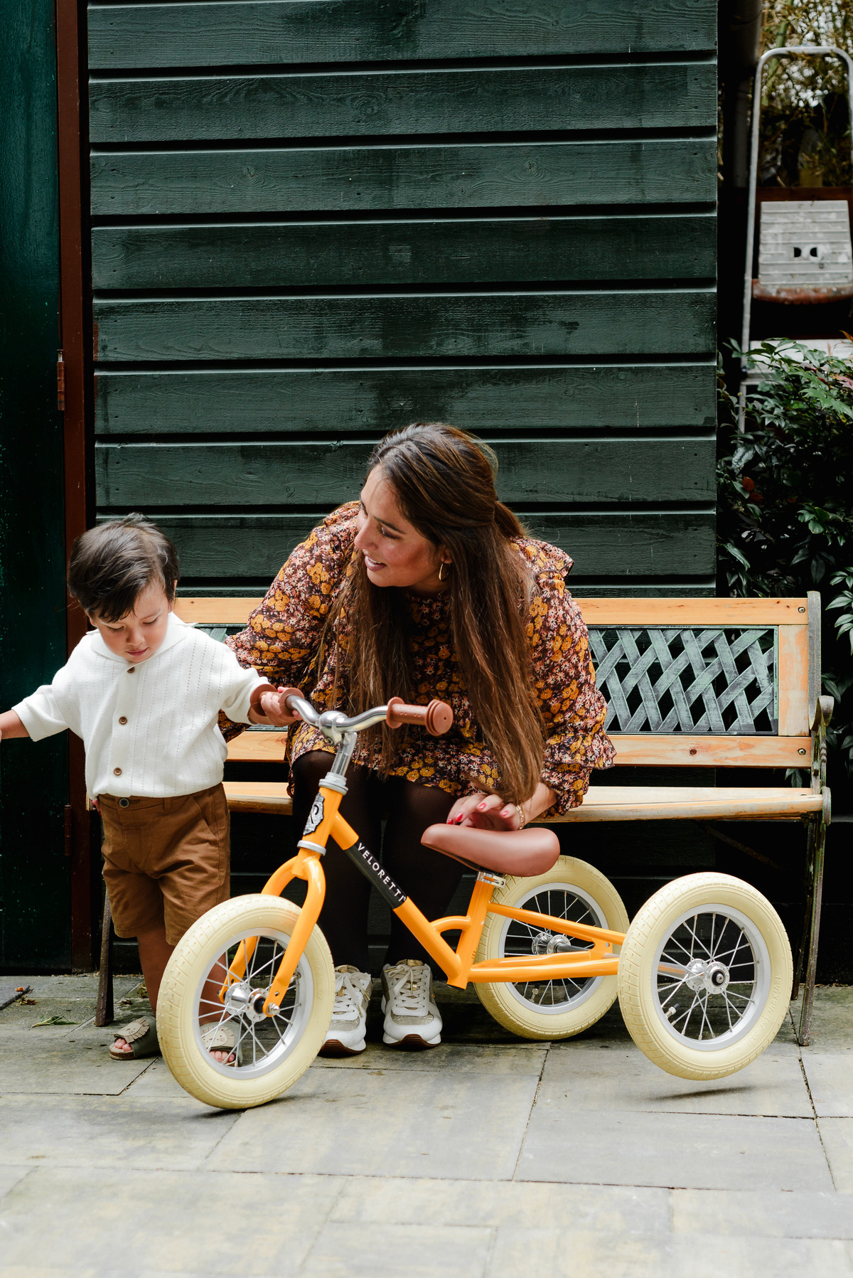 Two-year-old boy riding his first bike outdoors during his jungle-themed birthday party, with a big smile on his face and family cheering nearby.