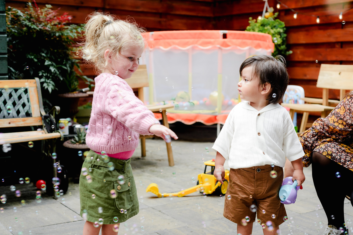 Kids playing together in the garden, laughing and chasing bubbles under the sunny sky.