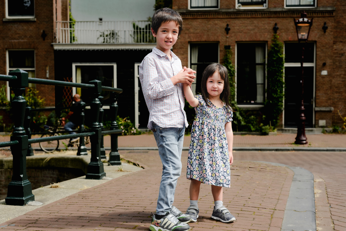 Kids posing on a charming Amsterdam bridge with colorful houseboats in the background.