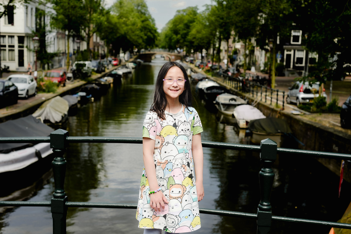 Kids posing on a charming Amsterdam bridge with colorful houseboats in the background.