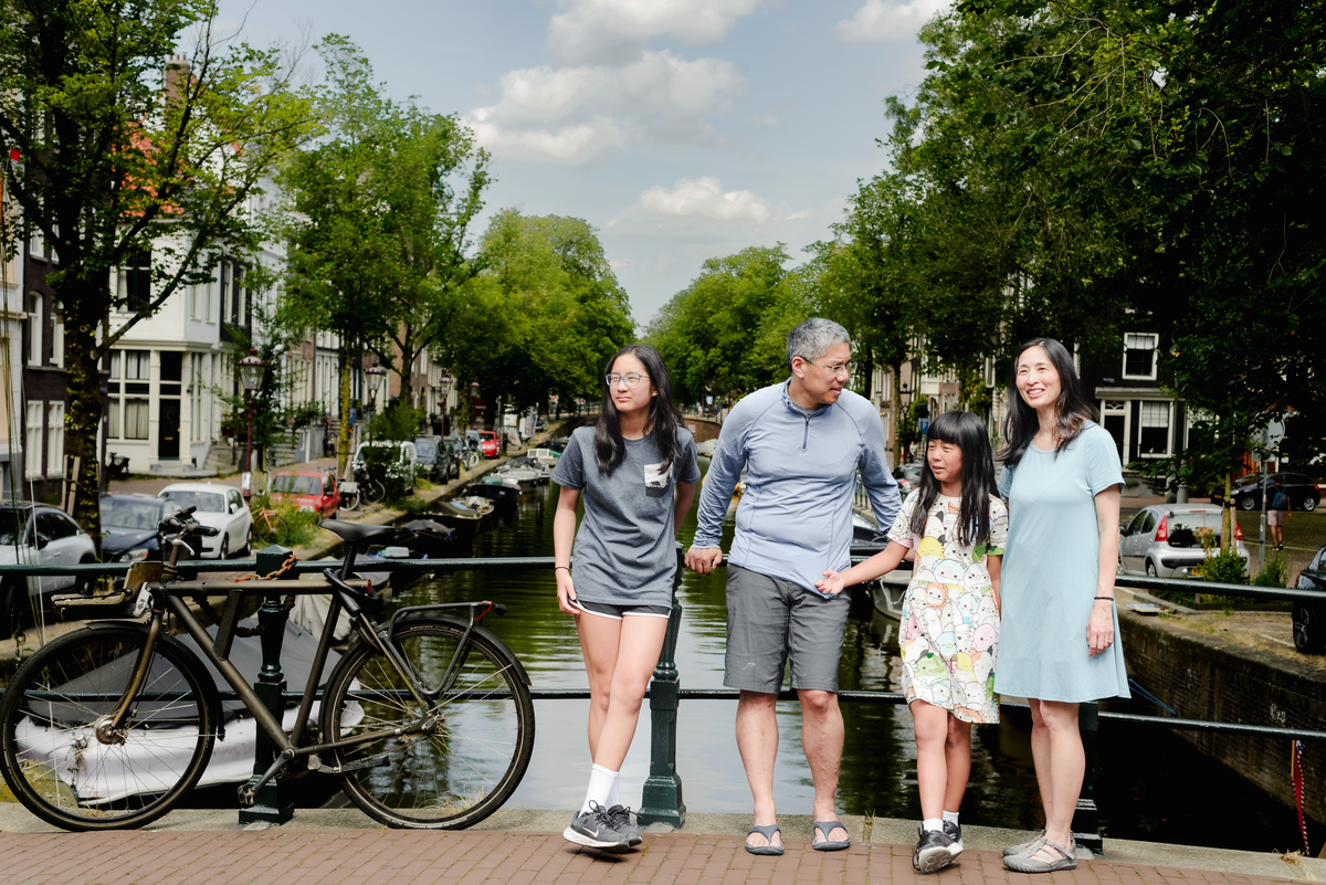 A family of four posing on a charming Amsterdam bridge with colorful houseboats in the background.