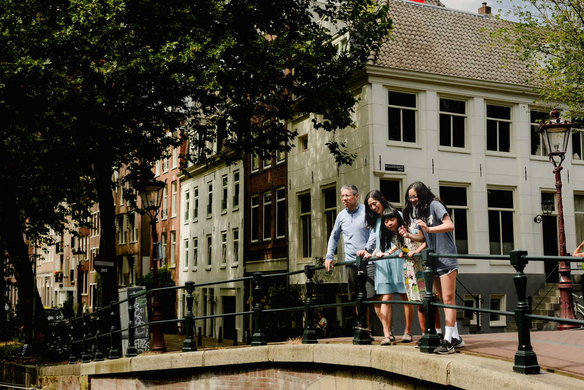 Family of four posing on a charming Amsterdam bridge with monumental houses in the background.