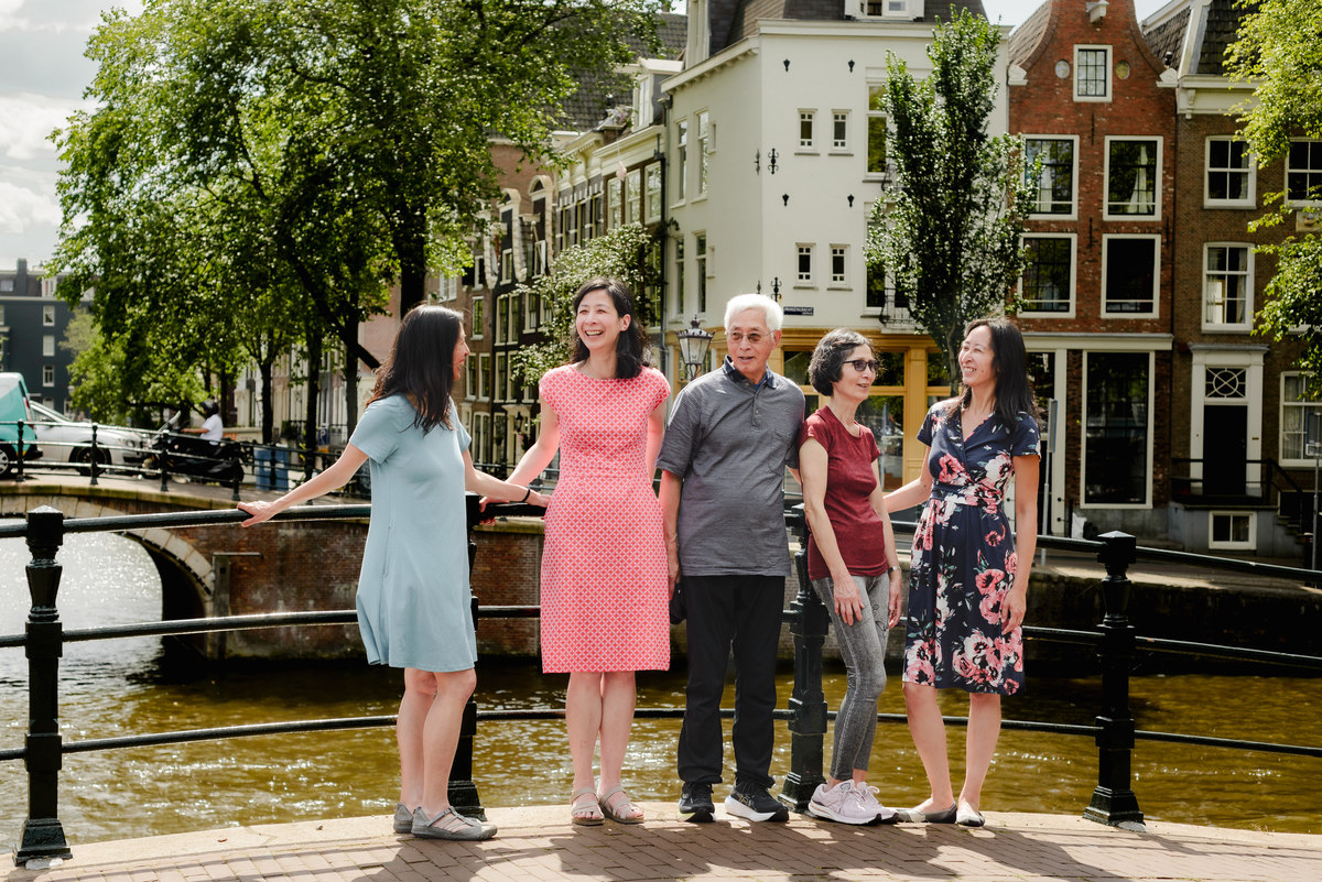 Grandparents standing with their three adult children, with the iconic canals of Amsterdam behind them