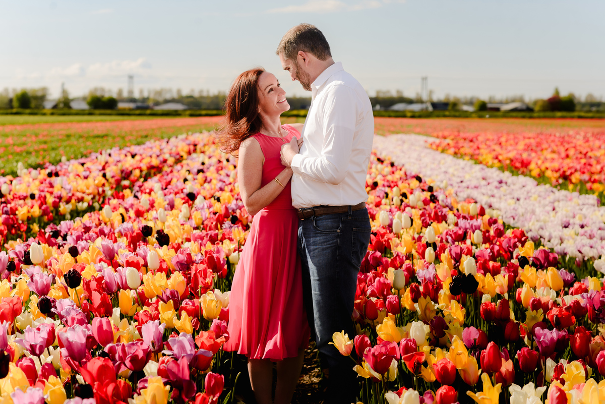  A woman leans into her partner’s embrace, eyes closed and smiling, as they stand surrounded by endless rows of colourful tulips