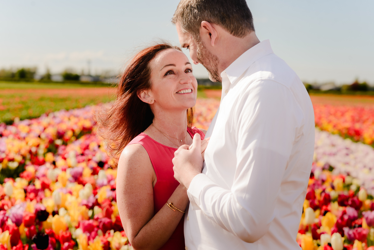  A woman leans into her partner’s embrace, eyes closed and smiling, as they stand surrounded by endless rows of colourful tulips