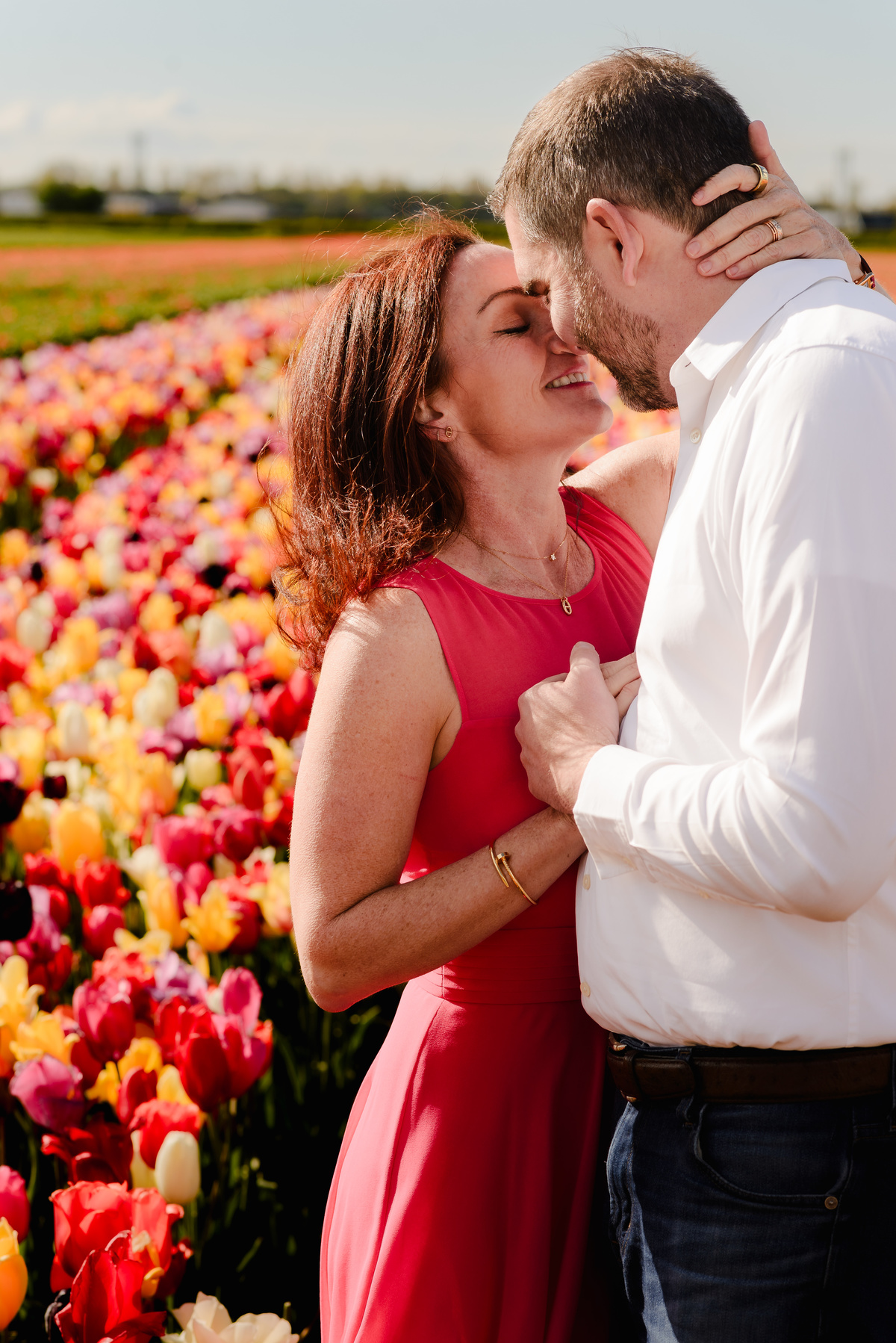  A woman leans into her partner’s embrace, eyes closed and smiling, as they stand surrounded by endless rows of colourful tulips