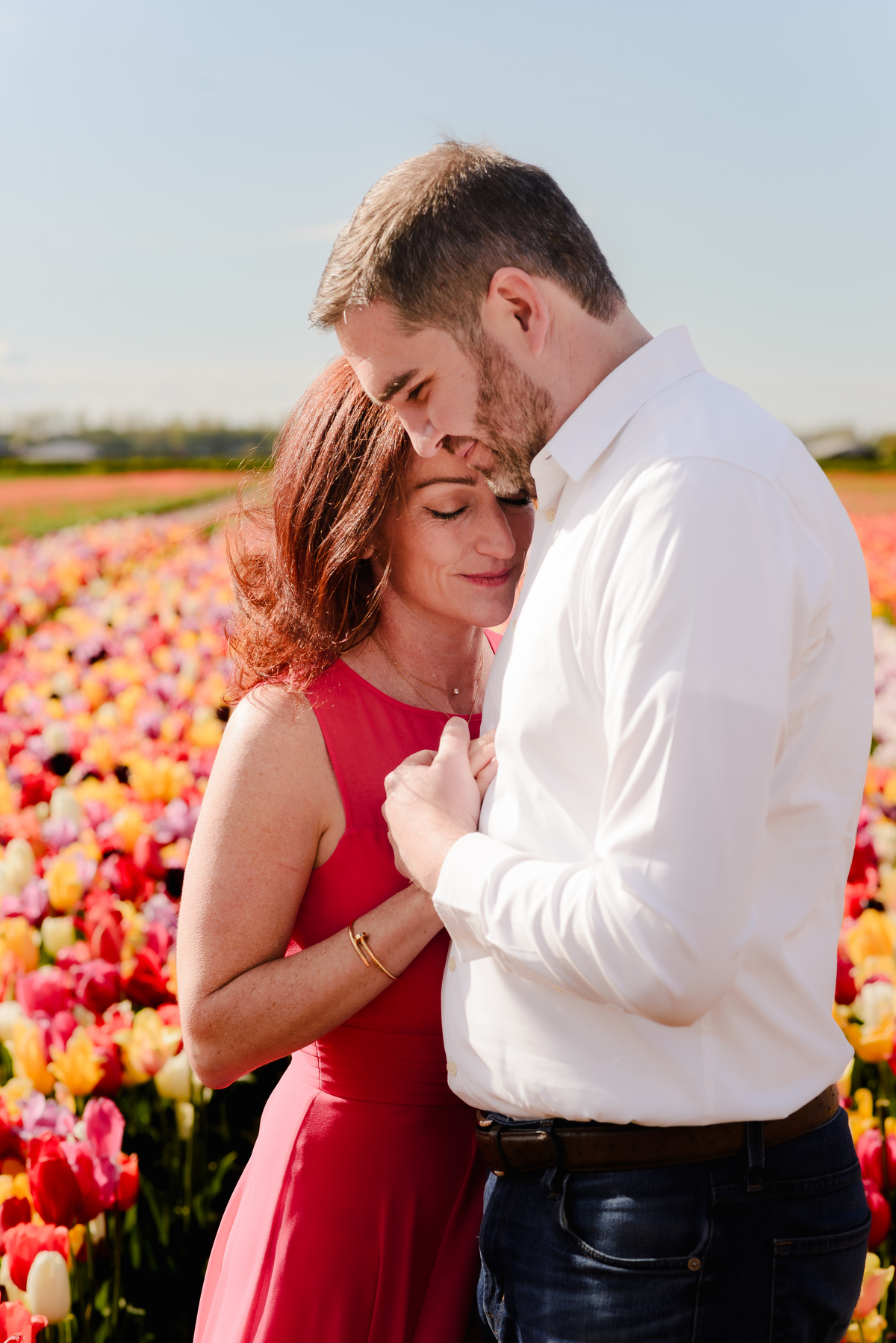  A woman leans into her partner’s embrace, eyes closed and smiling, as they stand surrounded by endless rows of colourful tulips