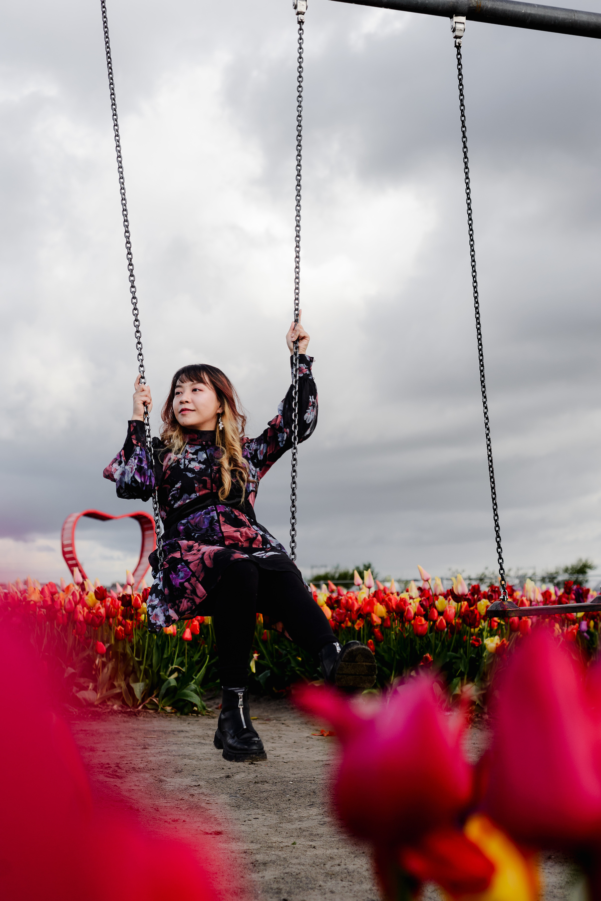 Woman sitting on a swing in a tulip garden, framed by colorful tulips and a cloudy sky, creating a playful and calm spring portrait.