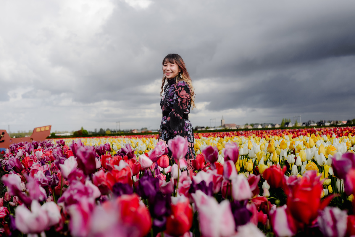 Smiling woman standing among colorful tulips in Hillegom with storm clouds overhead, capturing spring atmosphere in the Netherlands.