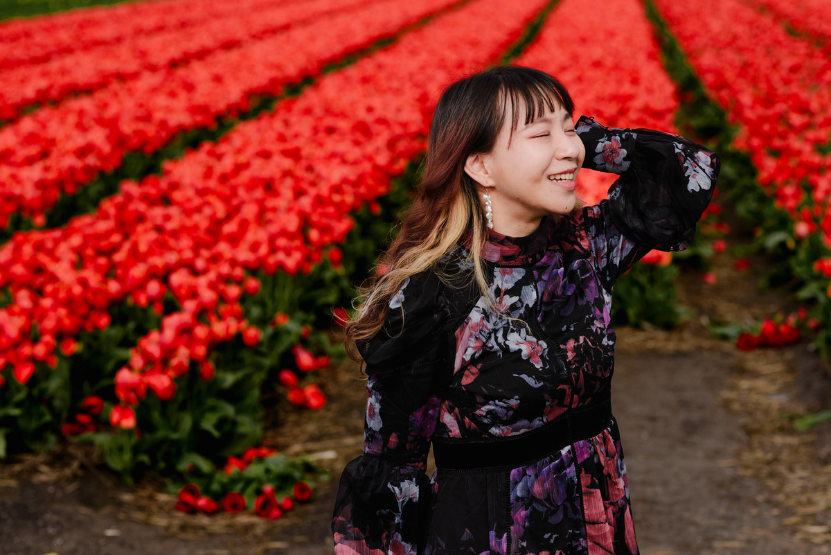 Woman smiling among red tulip fields in Hillegom, photographed during spring with shallow depth of field.