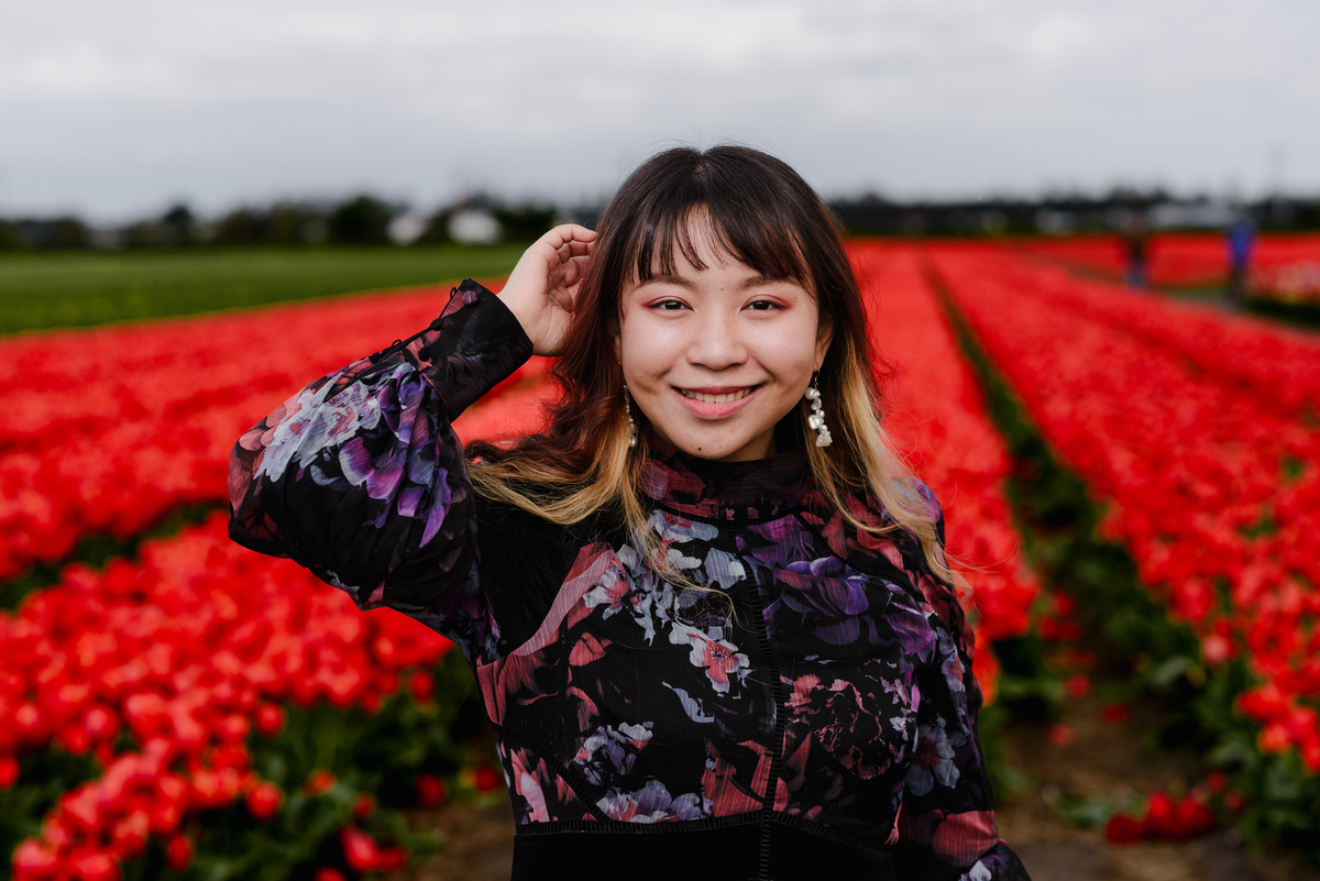Portrait of a woman smiling directly at the camera with red tulip fields stretching behind her in Hillegom.