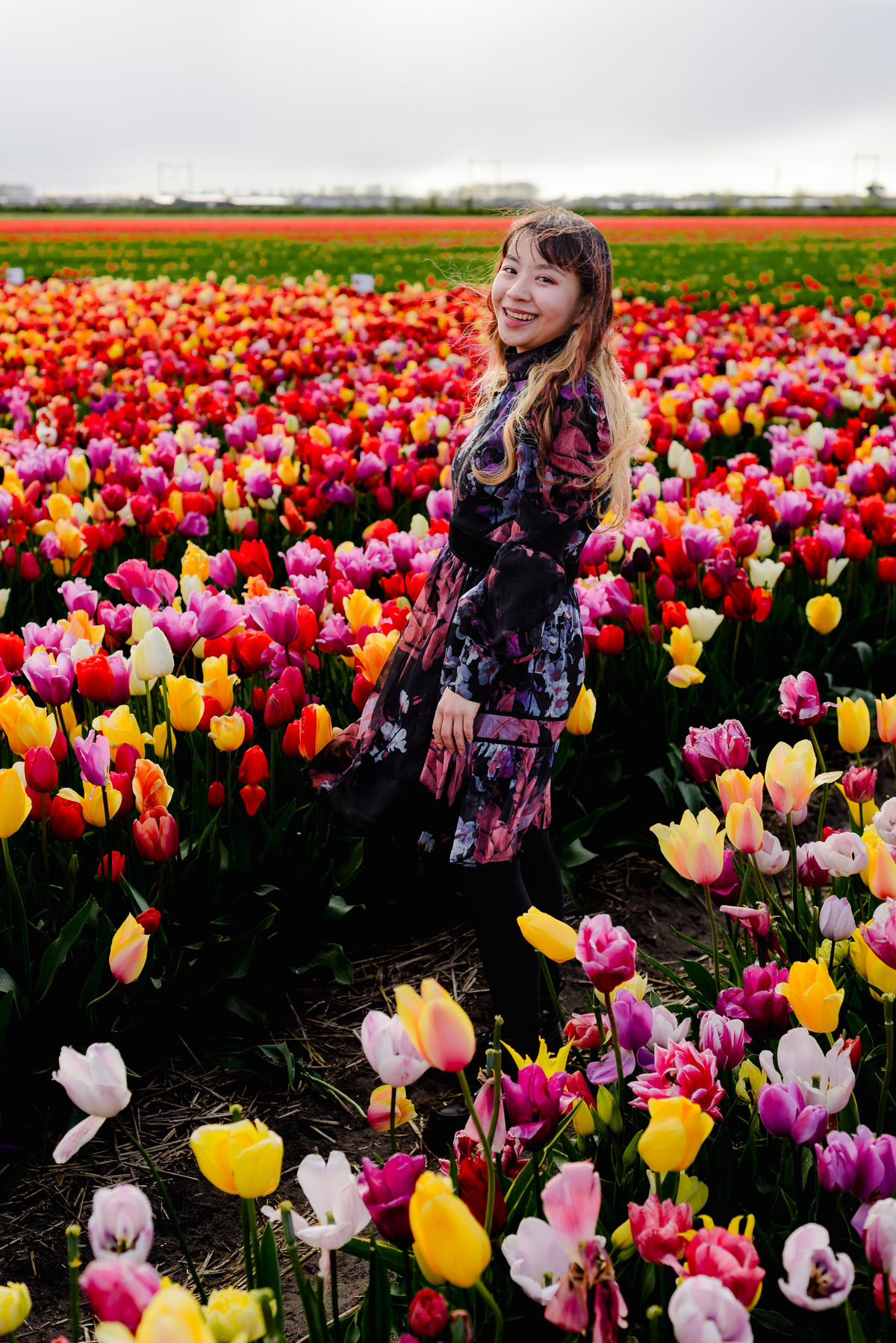 Smiling woman standing among colorful tulips in full bloom in Hillegom, photographed after rain with soft light.