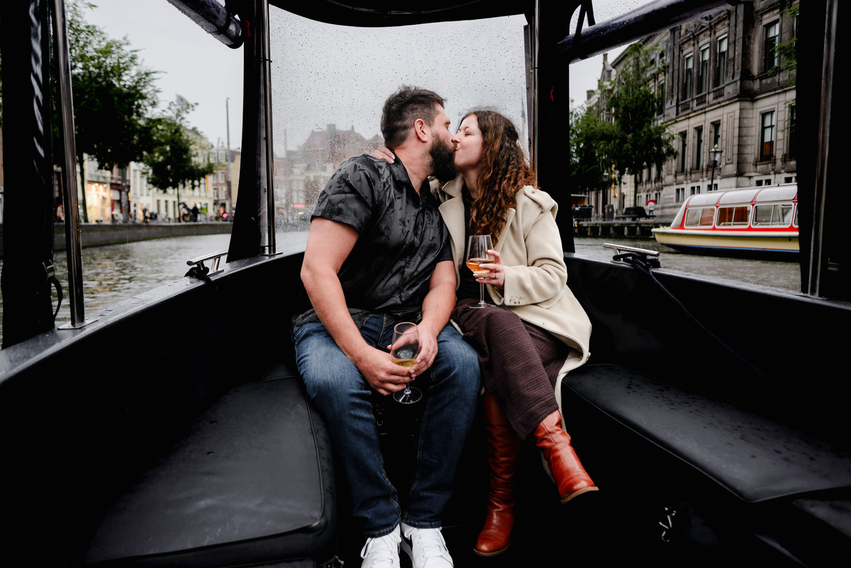 Engaged couple laughing and holding hands on the deck of a boat, surrounded by Amsterdam’s beautiful waterways.