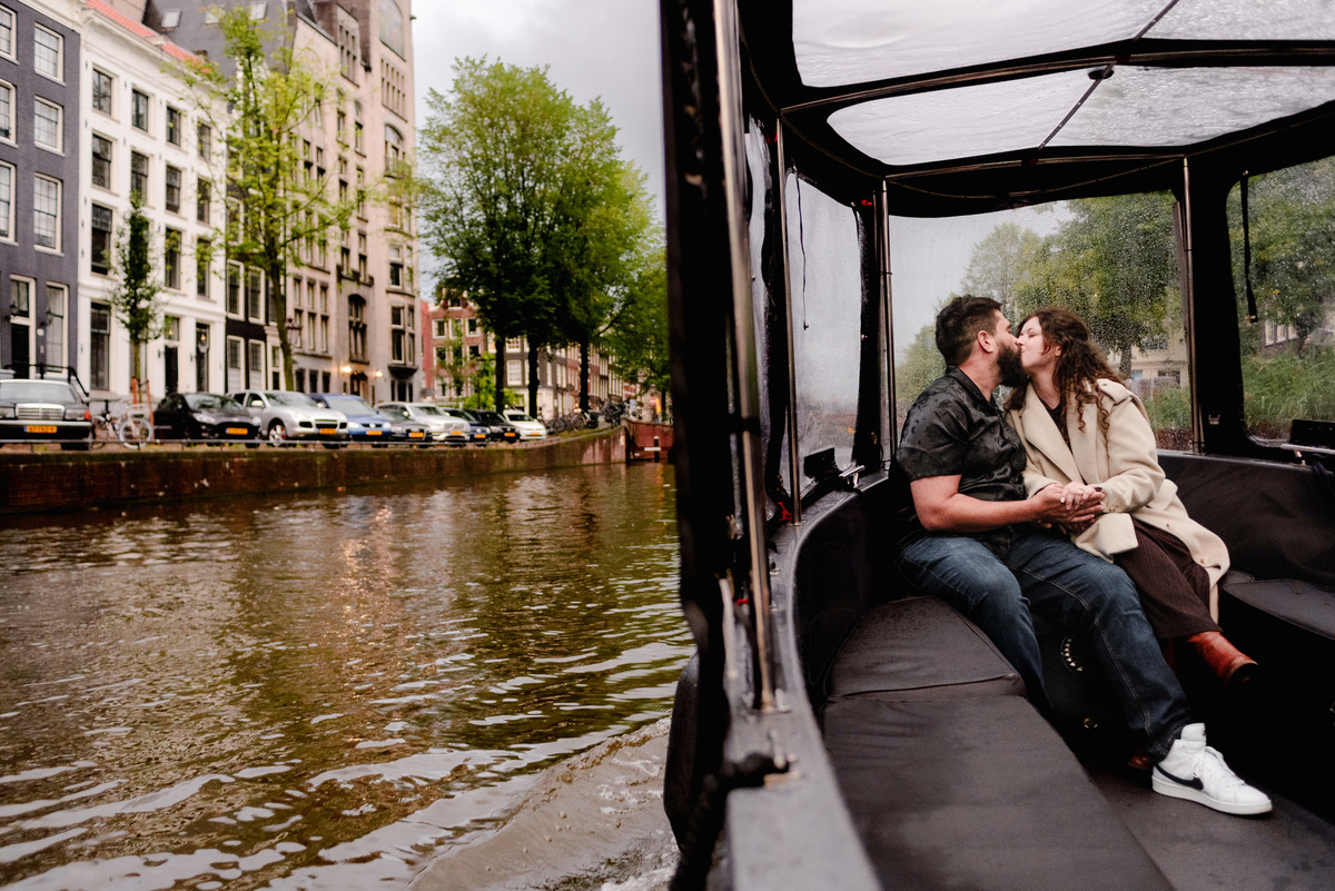 Engaged couple laughing and holding hands on the deck of a boat, surrounded by Amsterdam’s beautiful waterways.