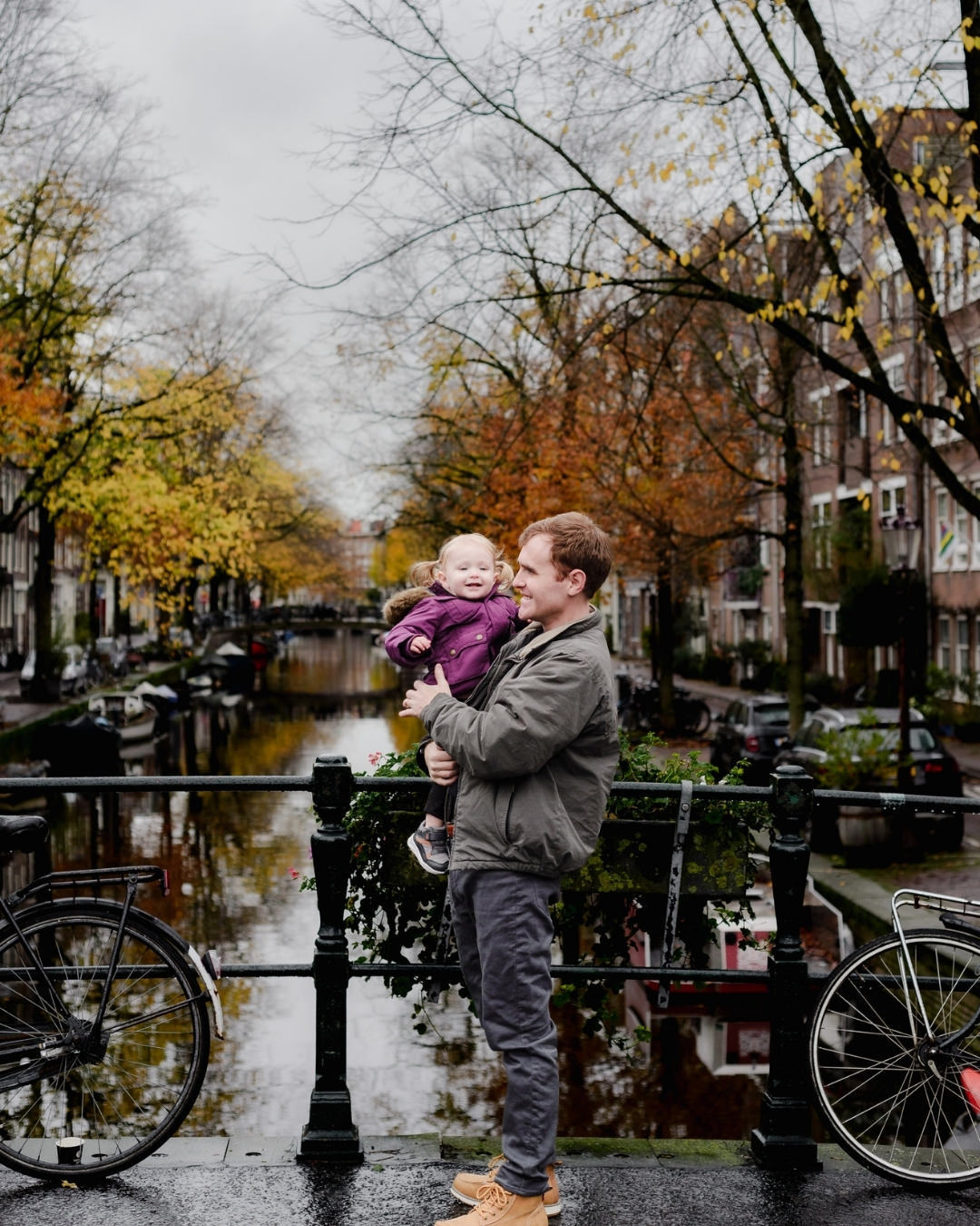 A father and daughter share a joyful moment on a canal bridge in Jordaan, Amsterdam, during an autumn photo session. With golden leaves and scenic reflections in the water, this image captures the warmth of family memories in the city's charming streets.