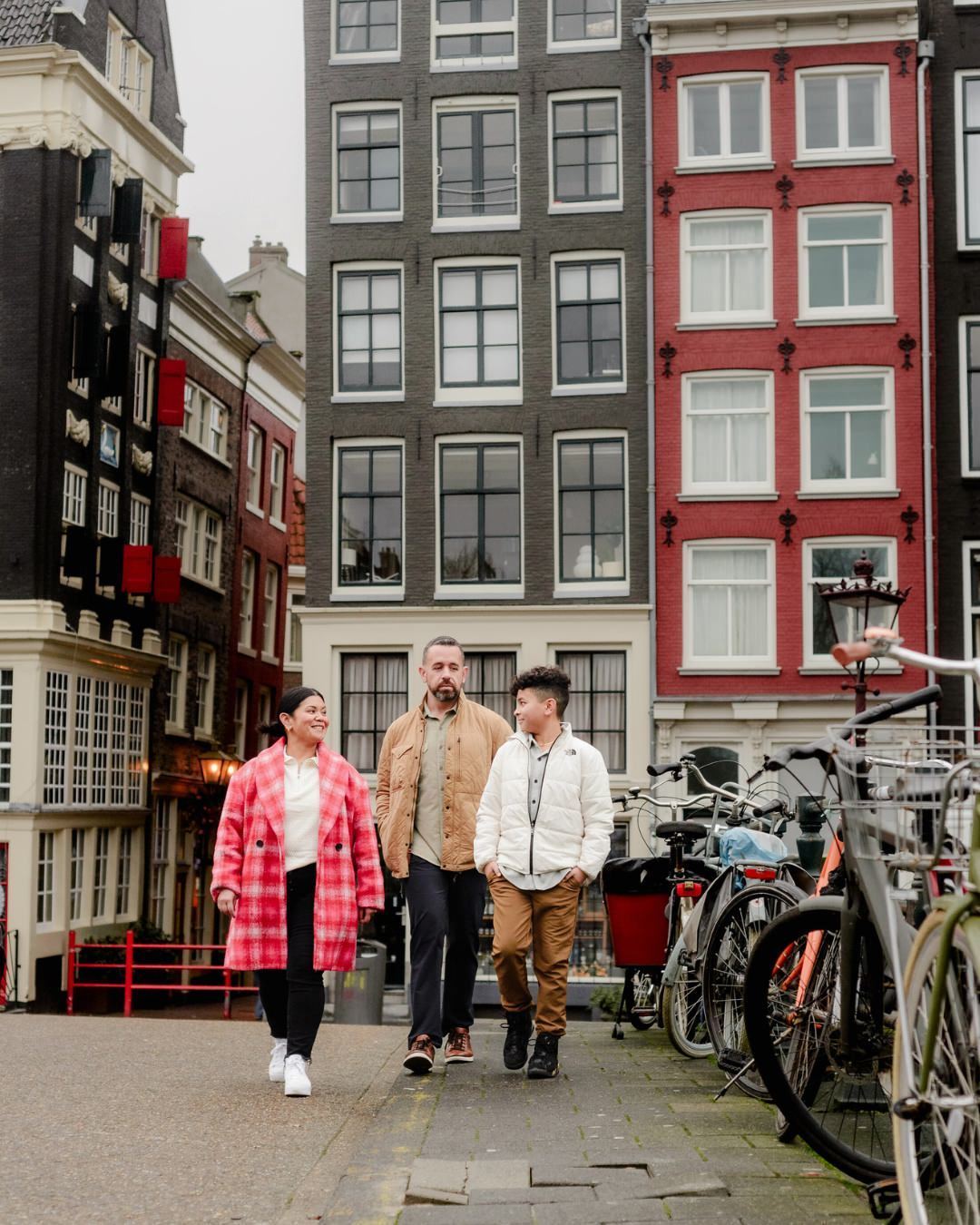 A family strolls along a classic Amsterdam street lined with bicycles and historic architecture. Their natural expressions and connection make this a timeless moment during their travel photography experience.