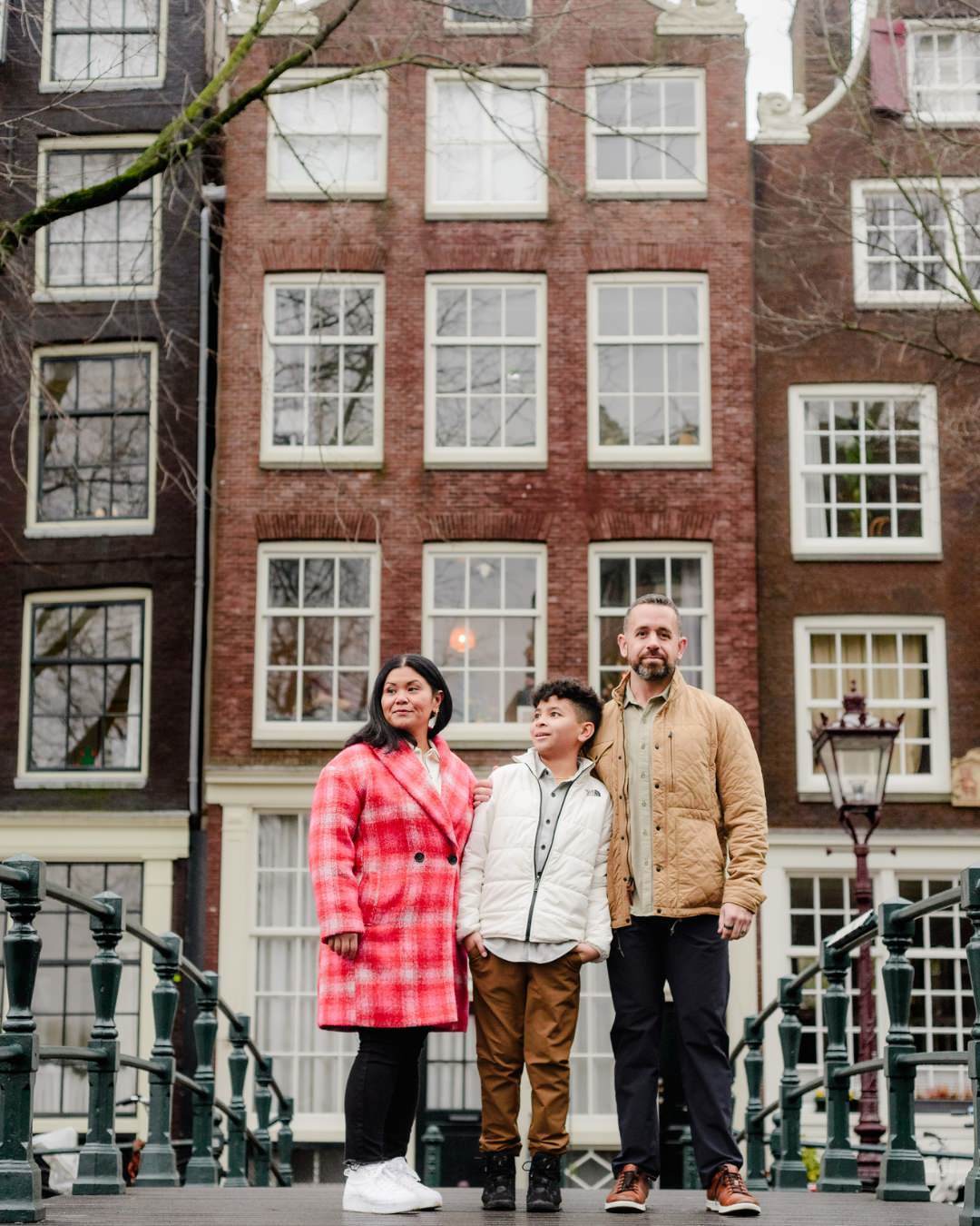 Standing on an iconic bridge, a family admires the historic facades of Amsterdam’s Canal Belt. The architecture and reflections in the water create a dreamy backdrop for this travel photography session.