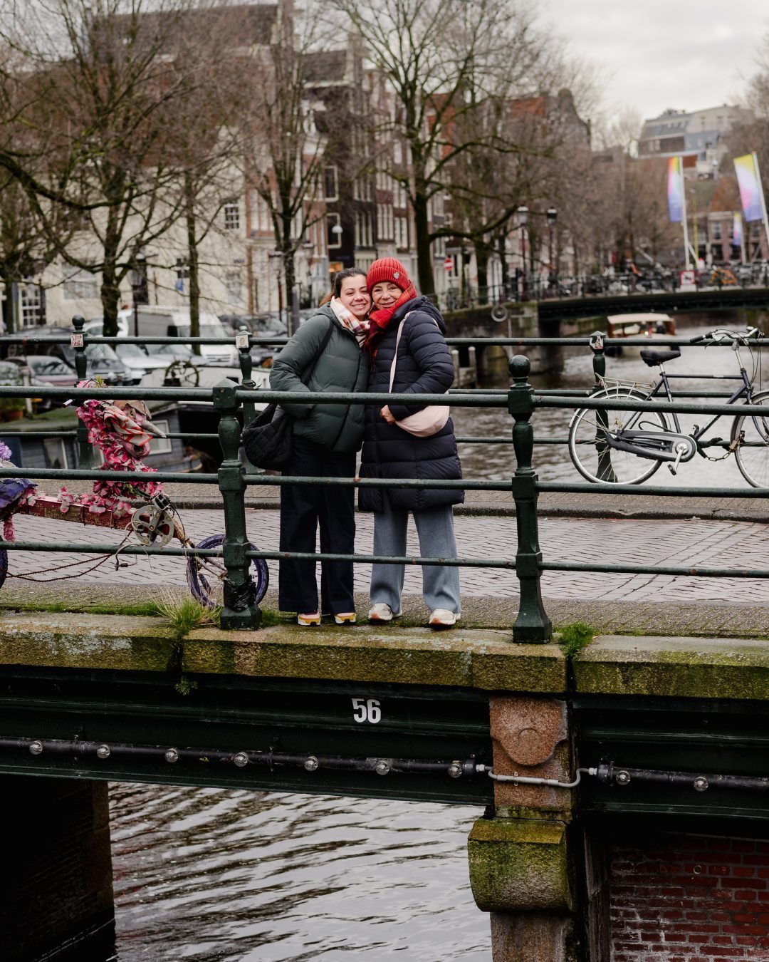 A Final Snapshot – Standing on a canal bridge, wrapped up in their winter layers, they take a final moment to soak in the beauty of Amsterdam, capturing a timeless memory.