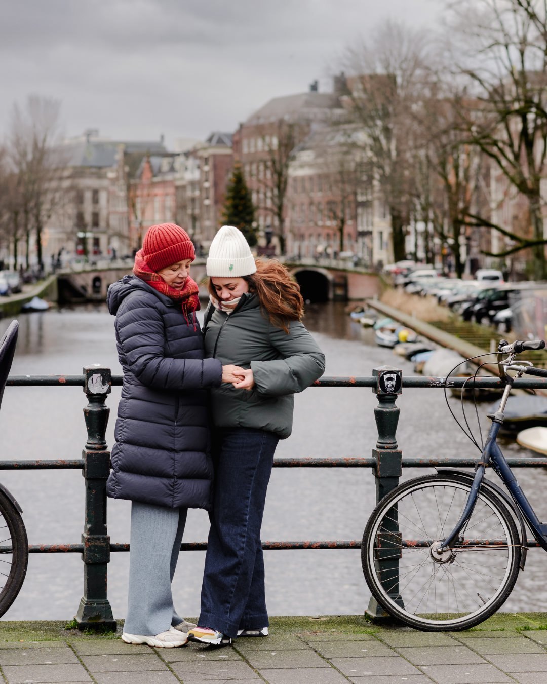 A Hug on the Bridge – With the canals stretching behind them, the daughter leans into her mother for a warm embrace, capturing the essence of their bond in the heart of Amsterdam.