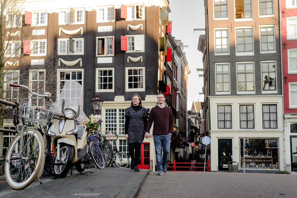 Couple walking hand-in-hand through a quaint Amsterdam street lined with colorful shutters and vintage bikes – perfect for a photo session with local flair.