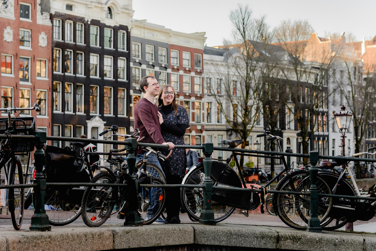 Smiling couple gazing into the distance on a charming Amsterdam bridge, showcasing the romance of a city stroll photoshoot.
