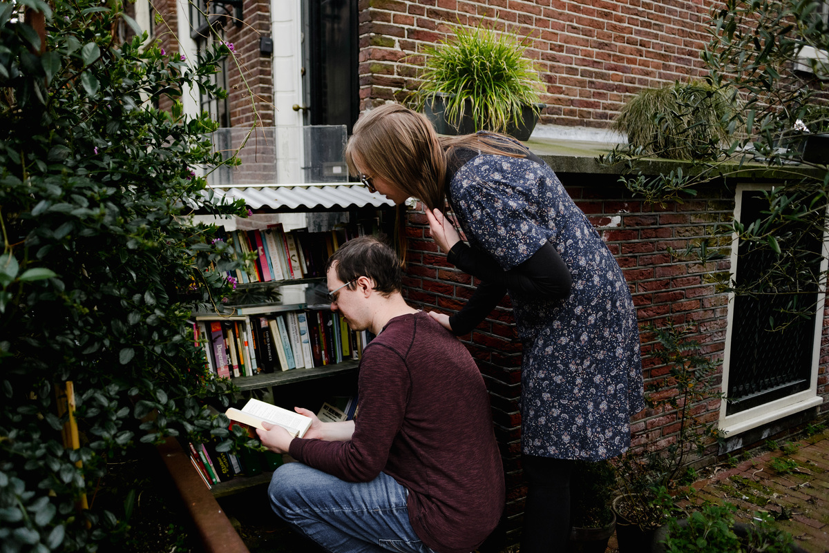 Authentic candid moment of a couple exploring a little free library during their Amsterdam couple photoshoot – a fun and personal city detail.