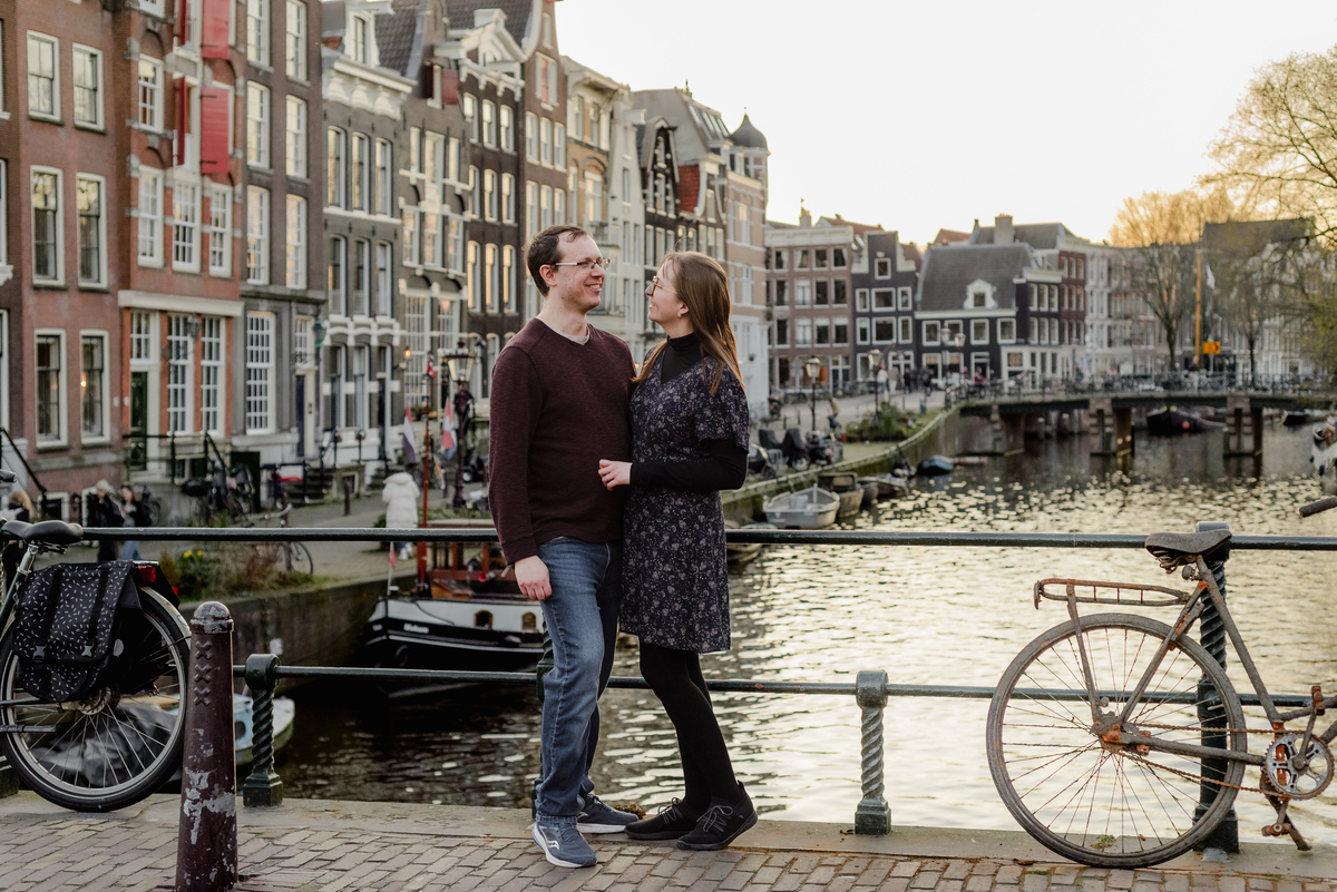Couple standing on a picturesque bridge in Amsterdam’s canal belt west, surrounded by historic Dutch architecture and peaceful waterways.
