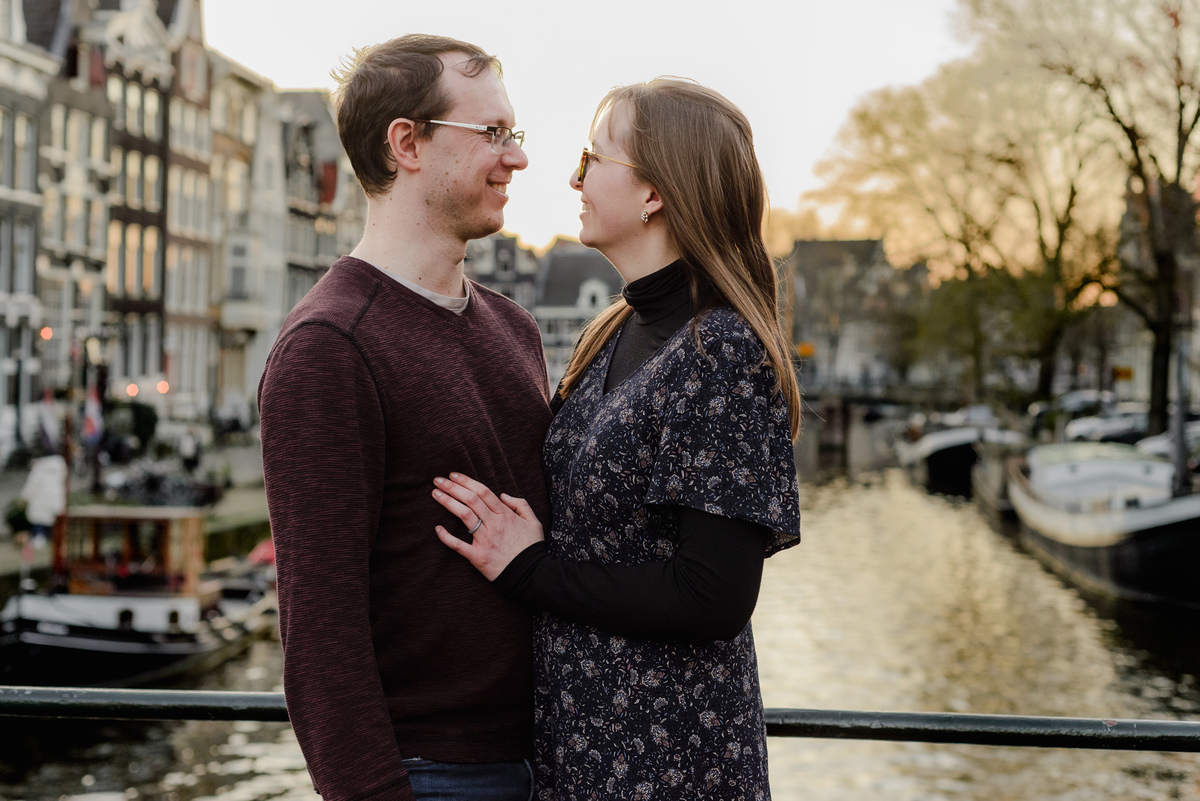 A romantic close-up of a couple smiling at each other during golden hour on an Amsterdam canal bridge – perfect for anniversary photo sessions in the city.