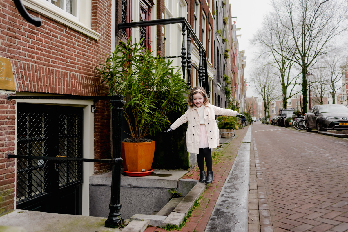 Childlike wonder captured as she explores a narrow stone ledge in the Jordaan, her smile full of adventure and joy.