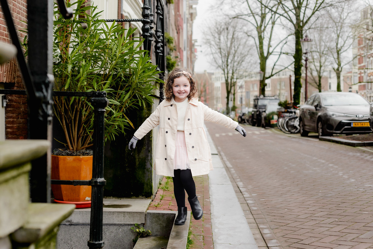 Childlike wonder captured as she explores a narrow stone ledge in the Jordaan, her smile full of adventure and joy.