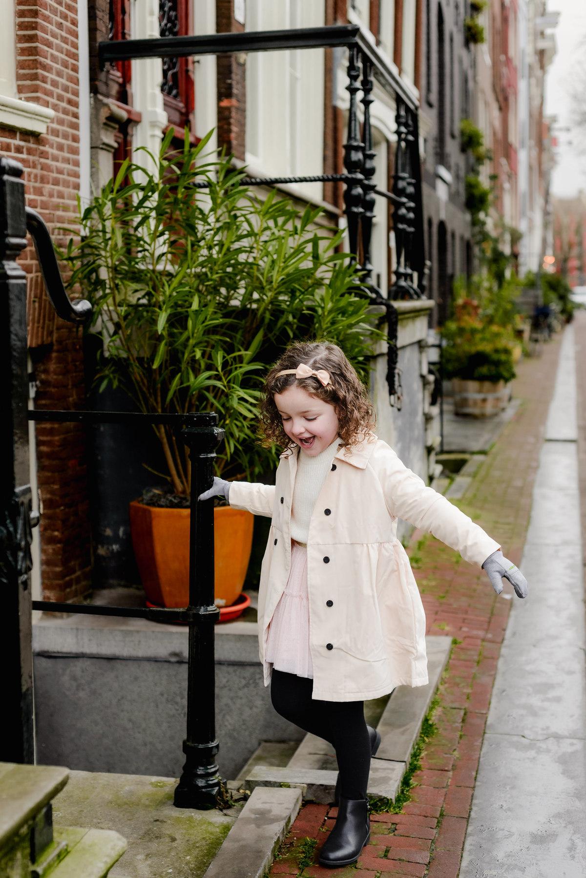 Playful street scene with the daughter walking a narrow ledge confidently, framed by charming Jordaan architecture.