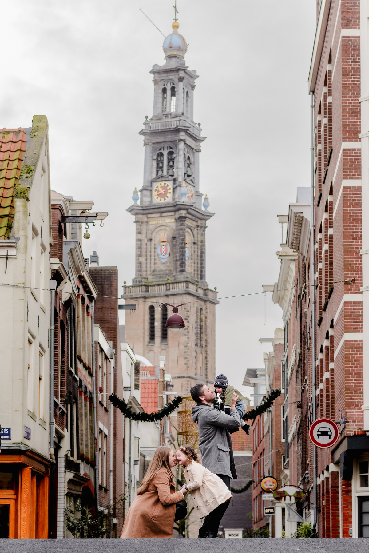 Sweet street-level family portrait in front of Westerkerk, as dad lifts baby and mom shares a moment with their daughter.