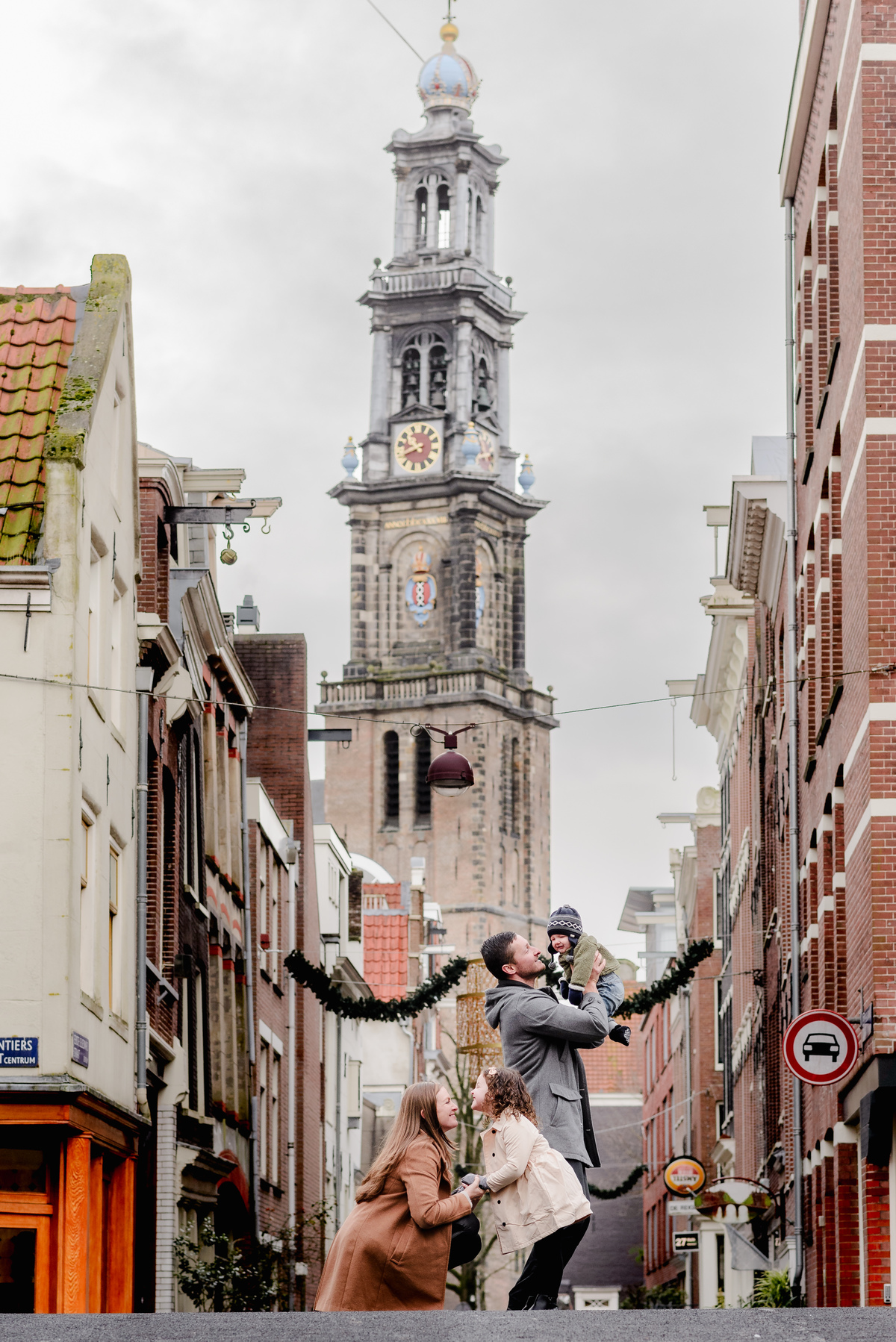 Playful family moment captured with the iconic Westerkerk tower rising high above, a symbol of Amsterdam in the background.