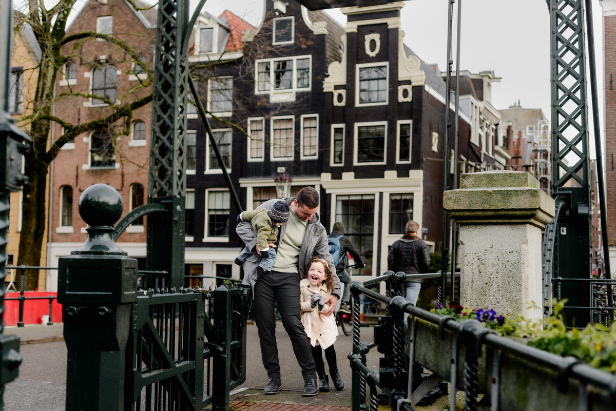 Joyful moment of a mother lifting her baby on a canal bridge in Amsterdam, while dad and daughter watch with smiles.