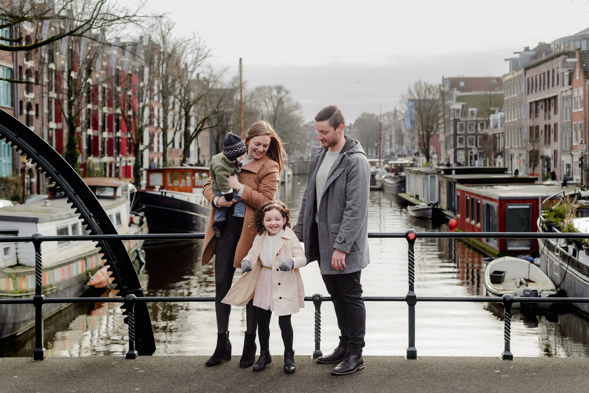 Family enjoying a sweet exchange with their daughter as they take in the view from a peaceful bridge over Amsterdam's canals.