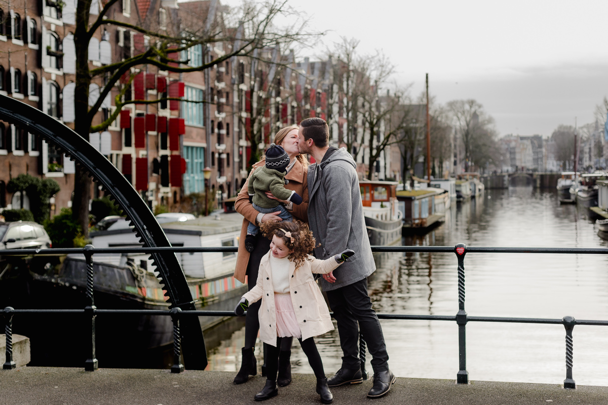 Lighthearted family moment on a bridge in Jordaan, with their daughter giggling and the canal scene bringing a storybook feel.
