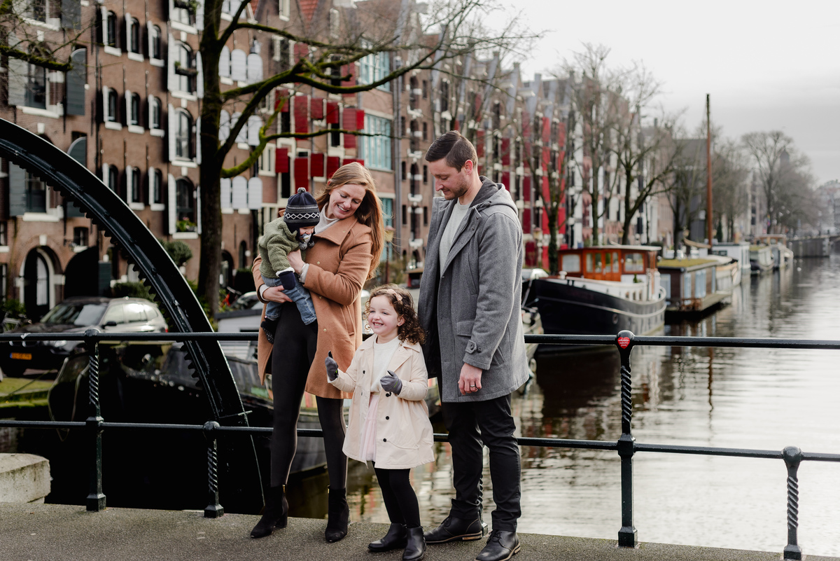 Mother lifts her bundled-up baby in the air while daughter cheers below during a wintery family photoshoot in Amsterdam.