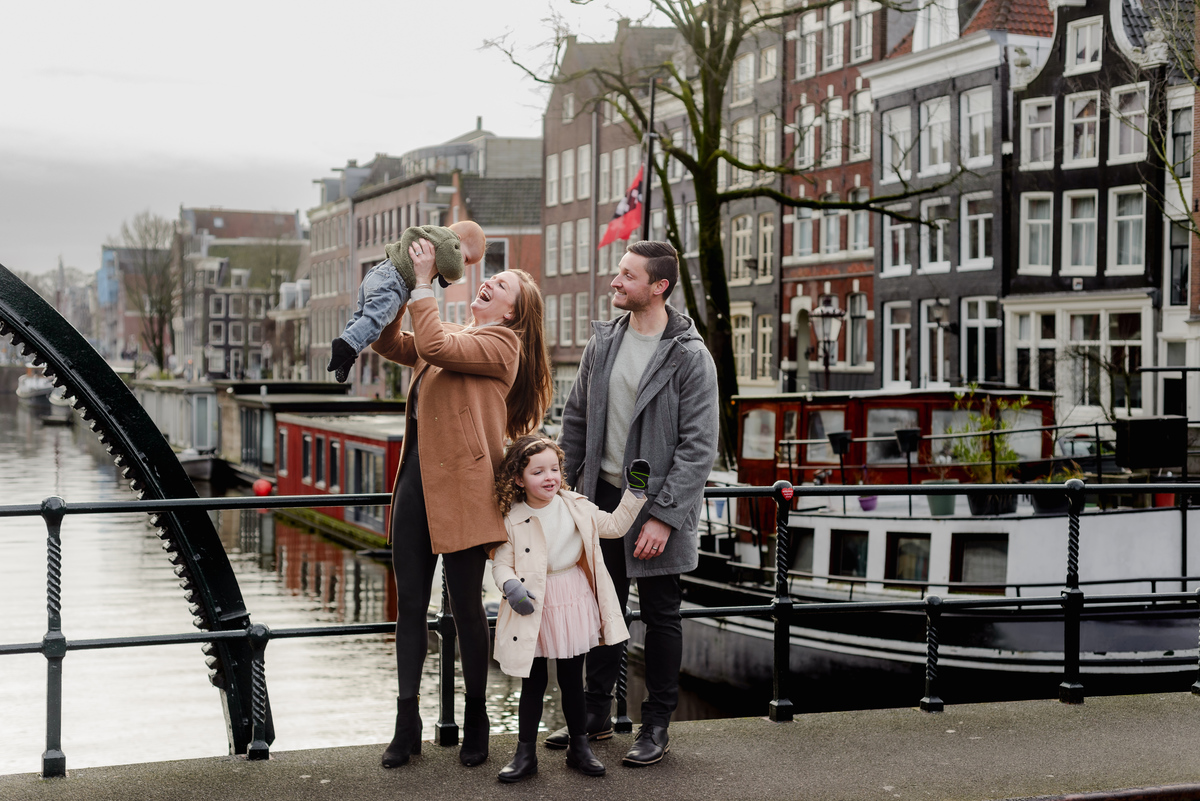 Joyful candid of a baby laughing as they're lifted into the air during a family session on a bridge in Jordaan, Amsterdam.