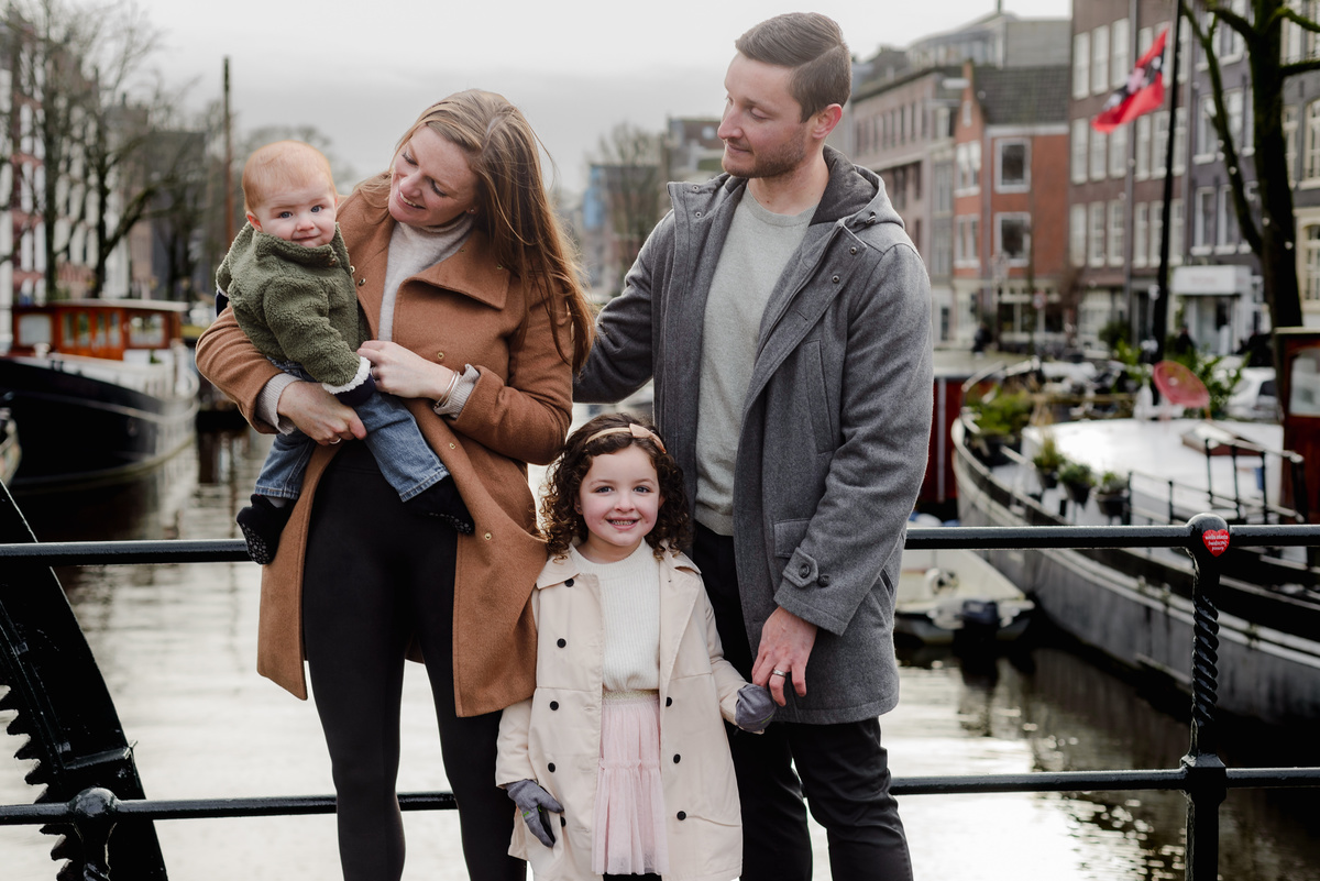 Fun behind-the-scenes moment of a family of four laughing and playing together near a canal bridge in Amsterdam.