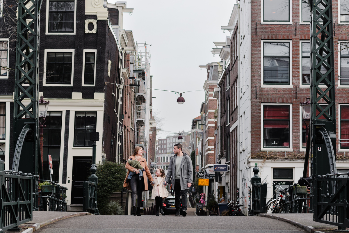 Portrait of a smiling family on an Amsterdam bridge, capturing love, laughter, and travel memories with their young children.