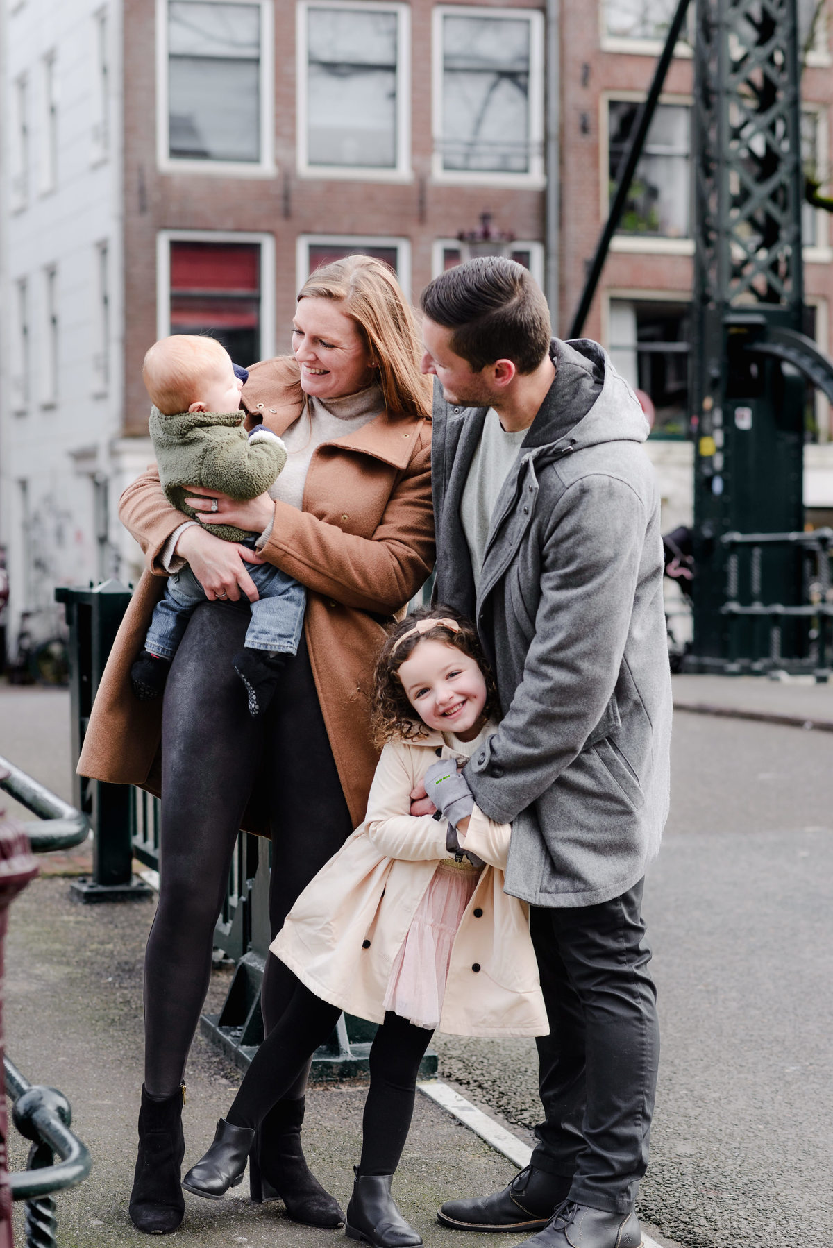 Portrait of a smiling family on an Amsterdam bridge, capturing love, laughter, and travel memories with their young children.