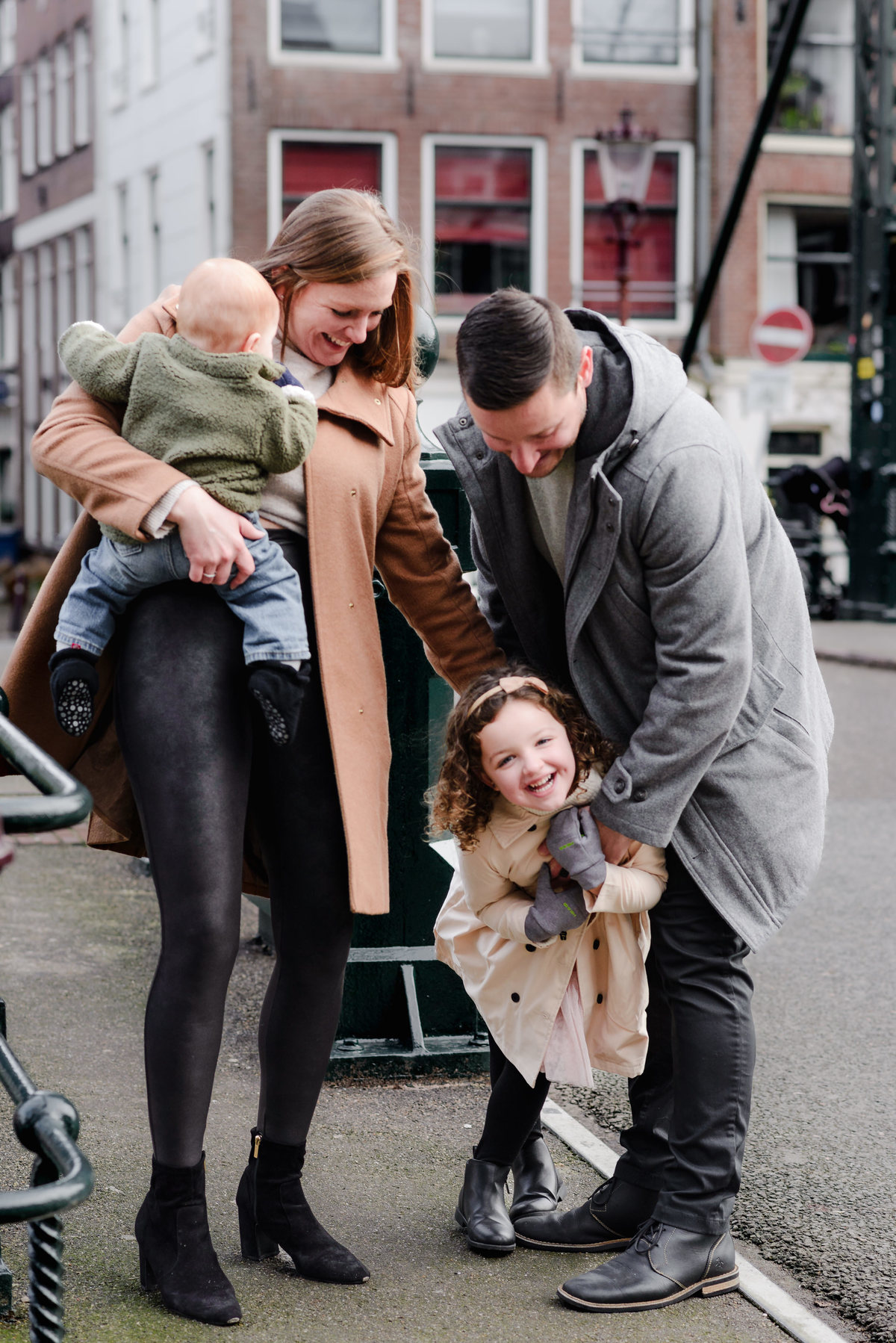 Fun behind-the-scenes moment of a family of four laughing and playing together near a canal bridge in Amsterdam.