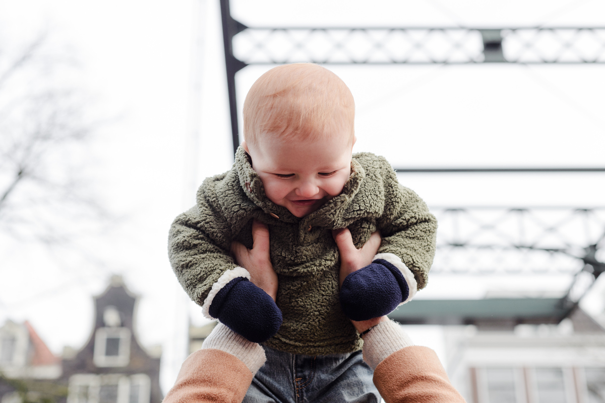 Joyful candid of a baby laughing as they're lifted into the air during a family session on a bridge in Jordaan, Amsterdam.
