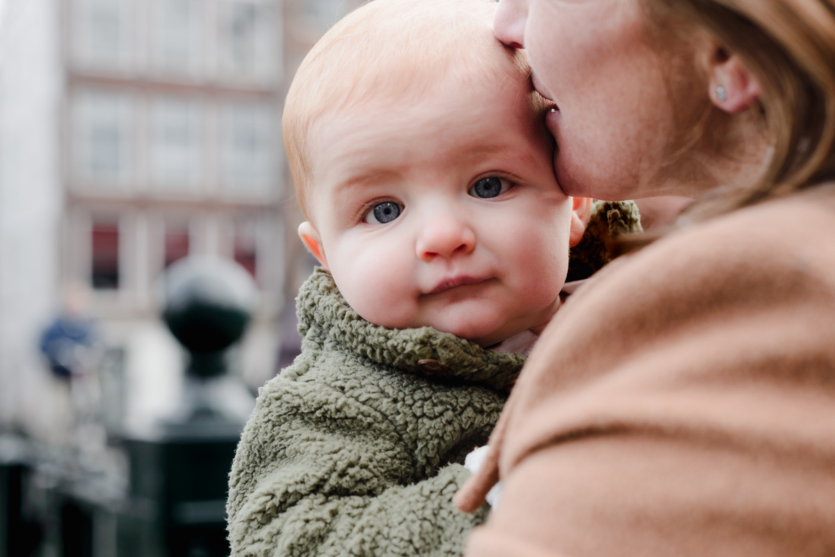 Sweet and intimate moment of a baby being kissed by mom while exploring the streets of Amsterdam during a family photoshoot.
