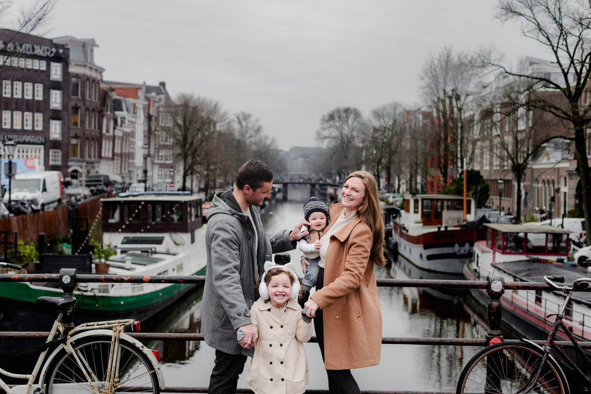 Snuggles, smiles, and cozy coats — this bridge moment radiates pure joy and love, with boats lining the canal behind.